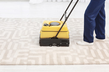 Male worker with carpet cleaner indoors, closeup