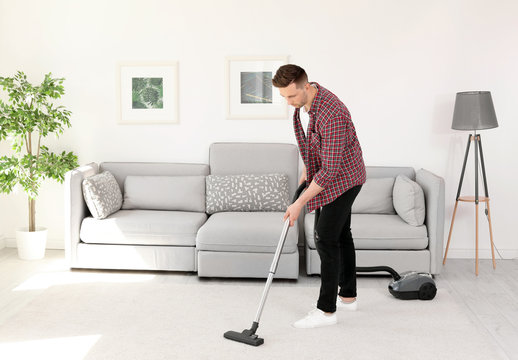 Young man removing dirt from carpet with vacuum cleaner at home