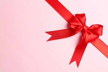 Red ribbon with bow on color background, top view