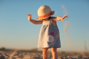 a little girl in a hat pours sand on the beach on a Sunny day