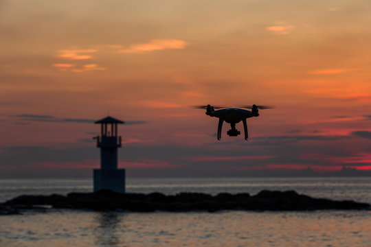 Silhouette of flying drone which taking photo over sunset sea