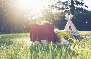 girl reading book in warm summer grass