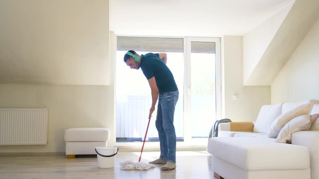 people, housework and housekeeping concept - happy man in headphones with mop cleaning floor at home