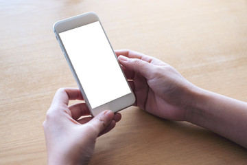Mockup image of hands holding white mobile phone with blank desktop screen on table in cafe