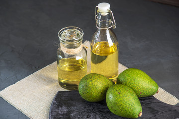 Avocado fruit and oil in glass bottle on dark background. Concept organic eco products for food and cosmetic procedures