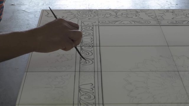Male hand tracing paint desing on white pottery tiles