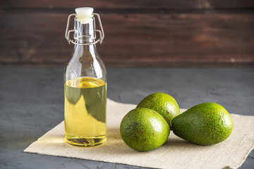 Avocado fruit and oil in glass bottle on dark background. Concept organic eco products for food and...