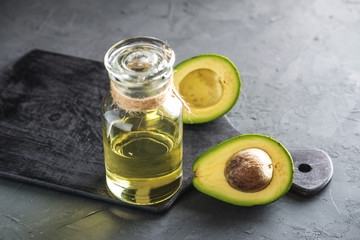Avocado fruit and oil in glass bottle on dark background. Concept organic eco products for food and cosmetic procedures