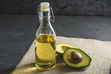 Avocado fruit and oil in glass bottle on dark background. Concept organic eco products for food and...