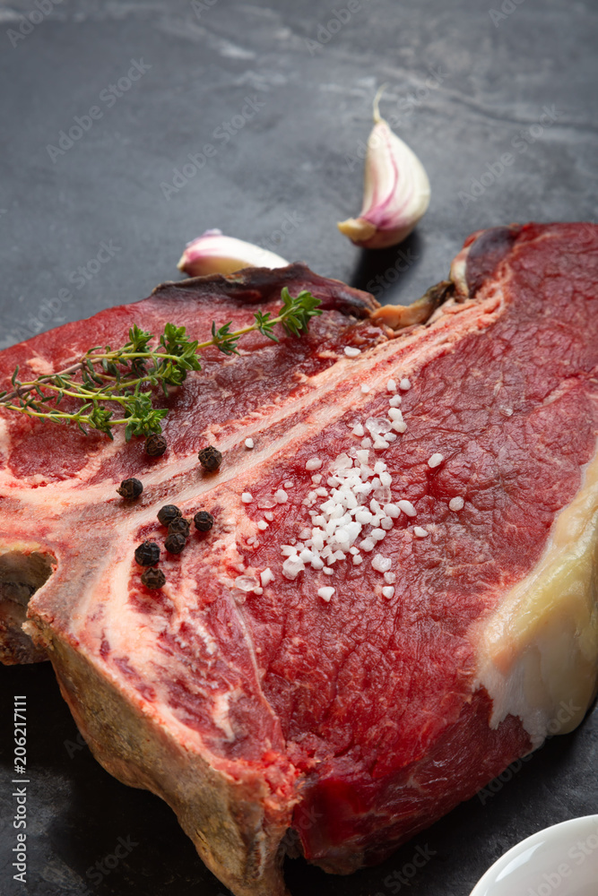 Wall mural Meat for a barbecue. One raw piece of beef meat on the bone. steak t bone, salt, spice, dark background view from above. The best piece of meat eight weeks maturation