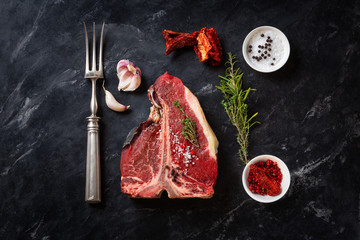 Meat for a barbecue. One raw piece of beef meat on the bone. steak t bone, salt, spice, dark background view from above. The best piece of meat eight weeks maturation