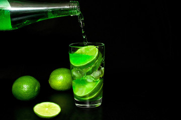 Glass of cold drink with ice and fresh ripe slice green limes on black background.