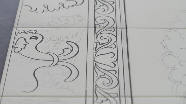 Male hand tracing paint desing on white pottery tiles