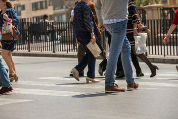 Fototapeta premium People stranded and distracted crossing the street in the pedestrian crossing at a busy intersection crowded and crowded in the midst of traffic only showing up the legs and feet. Walking and talking 