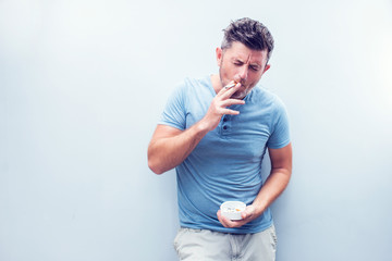 Handsome young man with brown hair wearing shirt isolated on grey background. Smoking cigarette.