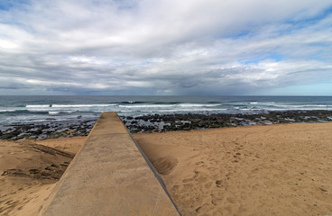 Concrete  Pipeline Extending onto  Beach and Rocky Coastal Seascape