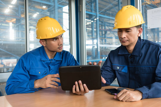 Two Asian skilled workers analyzing information displayed on tablet PC while sitting down indoors