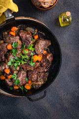 Pork cheeks stewed with vegetables in an iron pan, sliced bread, olive oil, with a dark background in a single shot above. Top view. Vertical copy space. Spanish food.