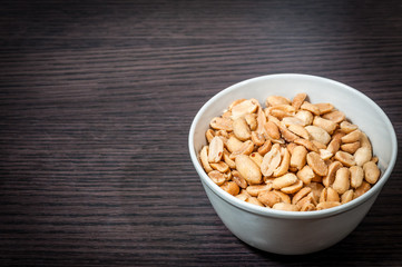 Roasted peeled salted peanuts in rustic bowl on wooden background
