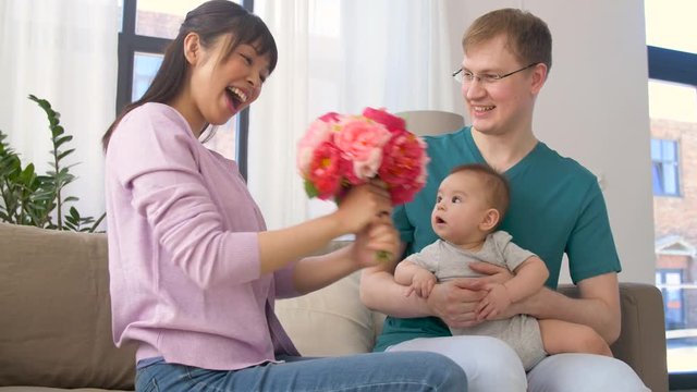 family, parenthood and mothers day concept - happy mother receiving flower bunch from father and baby boy at home