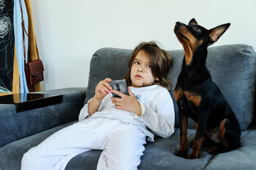 The girl with a smartphone on a sofa with a dog.