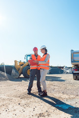 Worker and engineer on earthworks construction site planning, woman and man