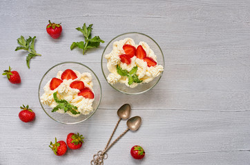 Homemade summer dessert with sliced strawberries and cream cheese in the glass bowls on a gray background with copy space. Decorated with vintage spoons and fresh mint leaves. Top view