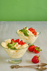 Parfait with sliced strawberries in the glass bowls on the gray kitchen table. Cold summer dessert decorated with fresh mint leaves and two vintage spoons. Side view