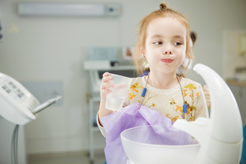 Fototapeta na wymiar Child rinses out mouth and sits in dentist chair