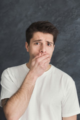 Frightened man covering mouth with hand at gray background