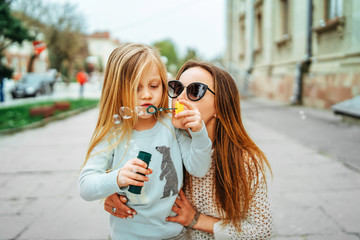 Little girl with mother blowing bubbles outdoor