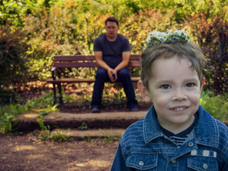 Father is sitting on a bench in a park and closing his eyes refusing to see that his son put a...