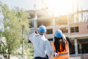 Asian man and woman engineer with the blue safety helmet meeting at the construction site with...