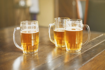 три стеклянные кружки со светлым пивом на деревянном столе