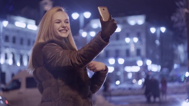 Happy young woman doing a selfie outdoor in night. beautiful smiling girl. Beautiful young woman taking selfie in the city
