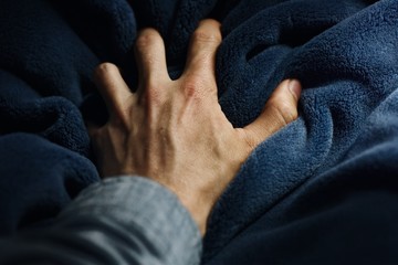 A frightened person's hand grabs a blanket nervously. - 206231308
