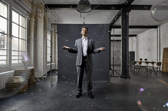 Mature businessman with bubbles standing in front of black backdrop in loft