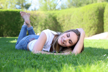 Hübsche blonde Frau mit nackten Füßen liegt mit geschlossenen Augen auf einem Rasen und lächelt