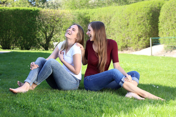 Zwei hübsche blonde Frauen sitzen auf einem Rasen und lachen ausgelassen