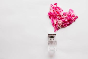 pink bottle of female perfume on a white background and heart made of petals of red and pink peonies, roses