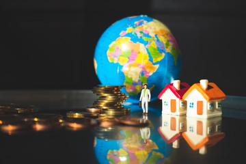Miniature people, businessman standing with stack coins and mini house on mini earth background using as business concept