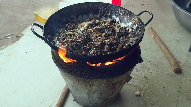  Woman using metal tongs to stir deep-frying frogs in a wok over a household stove ( close up 