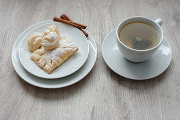 Puff pastry with sweet filling with powdered sugar on a white plate cup of tea and vanilla sticks on a wooden background