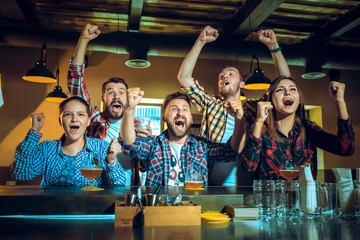 Sport, people, leisure, friendship and entertainment concept - happy football fans or male friends drinking beer and celebrating victory at bar or pub