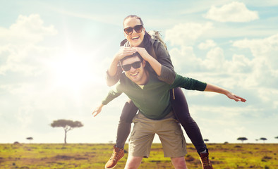 travel, tourism and people concept - happy couple with backpacks having fun over african savannah background