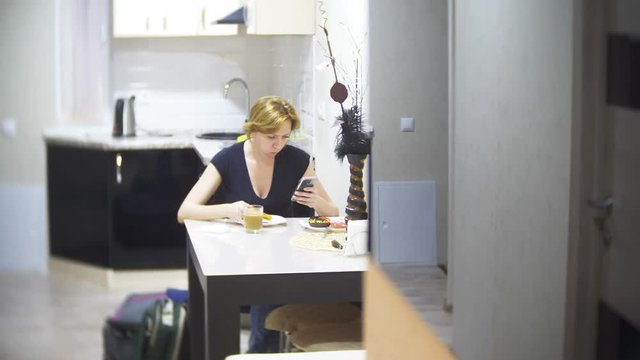 woman is eating pizza in the kitchen at home and using her smartphone, 4k, background blur