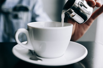 The guy pours cream into a white Cup of coffee.Morning coffee