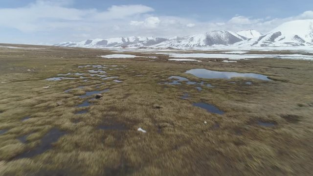 Fast Flying over Small Lakes with Ice Blocks in Spring. Snowy Mountains on Background. Aerial Low Angle View. Arabel Plateu. Kyrgyzstan