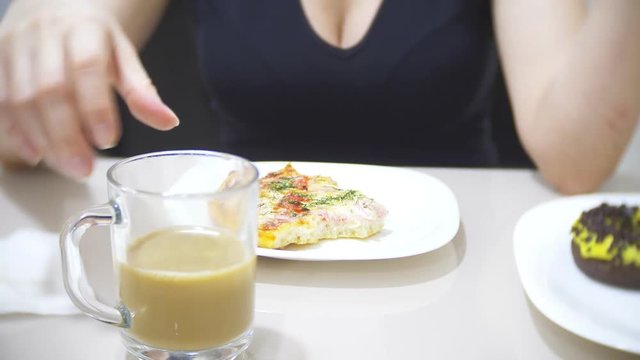 woman is eating pizza in the kitchen at home and using her smartphone, 4k, background blur