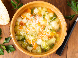 bowl of minestrone soup with toast on rustic wooden background, top view.